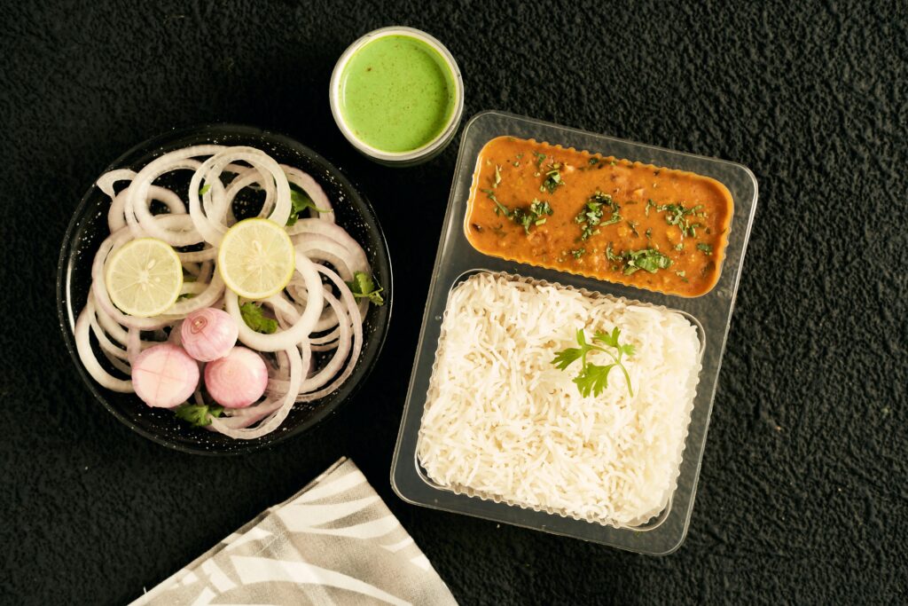 Delicious Indian meal featuring daal, white rice, onion salad, and green chutney from a top view perspective.