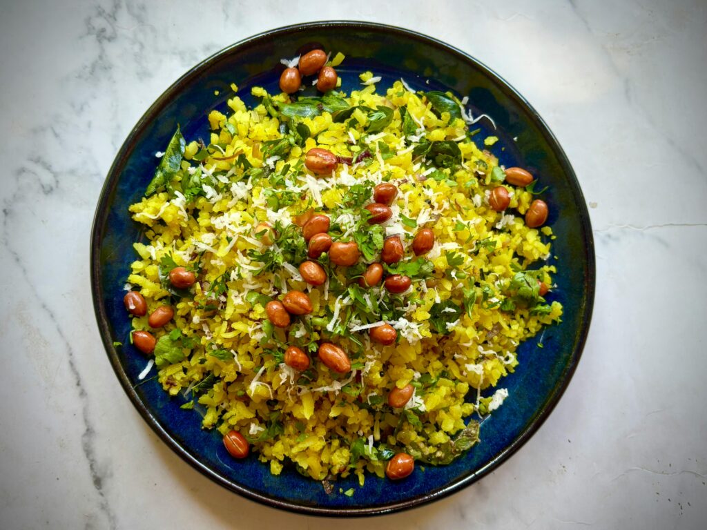 Delicious Indian poha with peanuts and herbs on a vibrant plate.